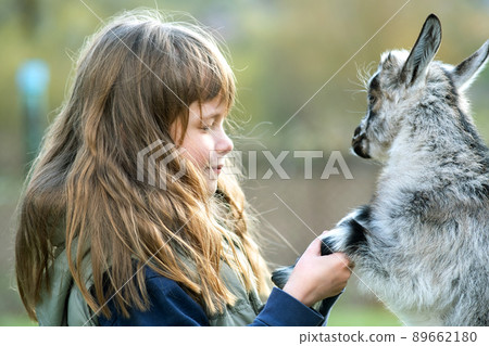 Pretty happy child girl playing with small kid goat at farm yard. 89662180