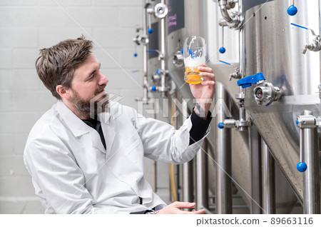 Brewer wearing white coat controlling process of beer fermentation while working at modern beer 89663116
