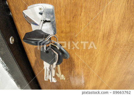 Close-up of bundle of different keys in key hole in wooden texture door. 89663762