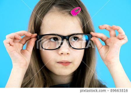 Close up portrait of a child school girl wearing looking glasses isolated on blue background. 89663816