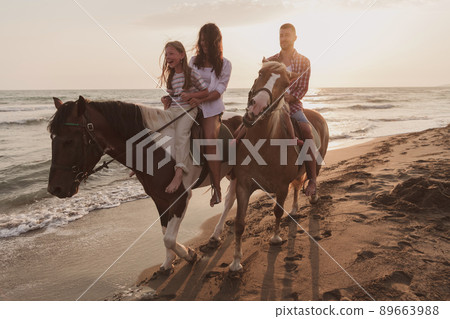 The family spends time with their children while riding horses together on a sandy beach. Selective focus The family spends time with their children while riding horses together on a sandy beach. Selective focus 89663988