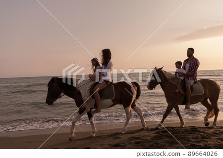 The family spends time with their children while riding horses together on a sandy beach. Selective focus The family spends time with their children while riding horses together on a sandy beach. Selective focus 89664026