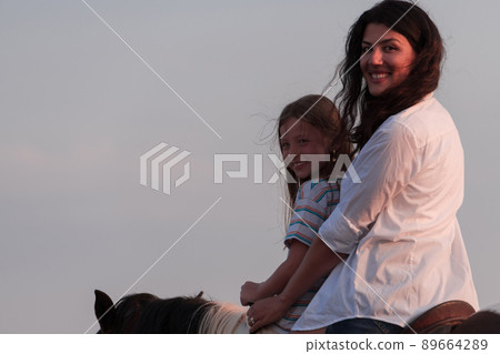 Mother and daughter enjoy riding horses together by the sea. Selective focus  89664289