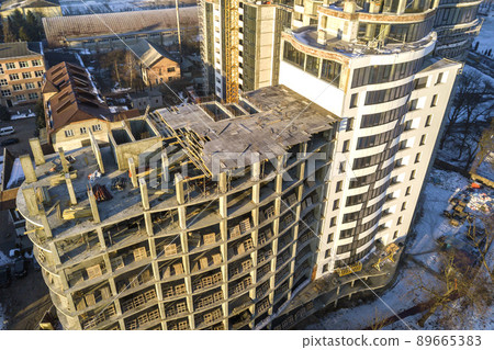 Aerial winter top view of modern developing city with tall apartment complex building under construction, parked cars, roofs and streets. Urban infrastructure, view from above. Aerial winter top view of modern developing city with tall apartment complex building under construction, parked cars, roofs and streets. Urban infrastructure, view from above. 89665383