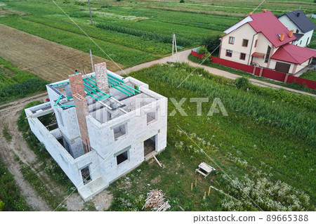 Aerial view of unfinished frame of private house with aerated lightweight concrete walls and wooden roof beams under construction. 89665388