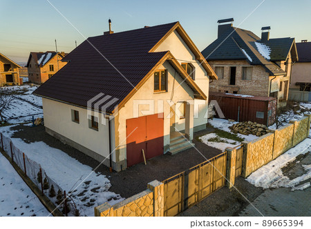 Aerial view of new residential house cottage and attached garage with shingle roof on fenced yard on sunny winter day in modern suburban area. Perfect investment in dream house. 89665394