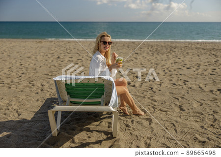 Woman on vacation smiling at camera, drinking cocktail and sunbathing on a deck chair 89665498