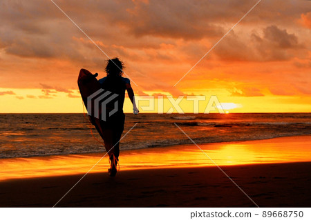 Silhouette of Young Surfer Man Carrying Surf at the beach with Amazing Sunset on Background. Bali 89668750