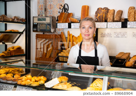 Female bakery employee offering bread and different pastry for sale Female bakery employee offering bread and different pastry for sale 89668904