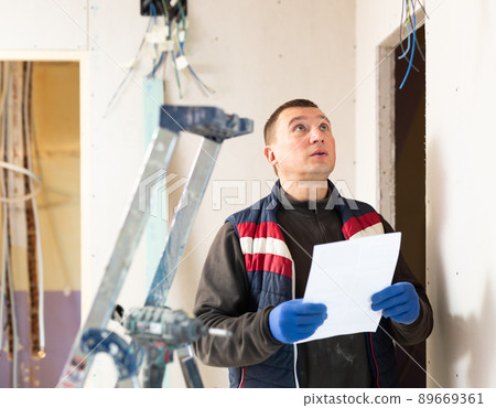 Builder standing at indoors building site, reading document 89669361