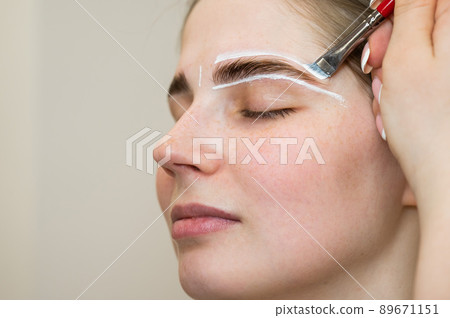 The master draws the shape of the eyebrows with white paint before coloring. The master draws the shape of the eyebrows with white paint before coloring. 89671151