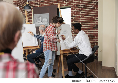 Class teacher explaining sketch process to young student during creativity school lesson. Diverse team drawing vase model on white canvas using illustration technique. Creative concept Class teacher explaining sketch process to young student during creativity school lesson. Diverse team drawing vase model on white canvas using illustration technique. Creative concept 89673730
