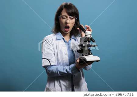 Microbiology expert with shock expression analyzing scientific discovery using modern microscope. Amazed researcher investigating bacteria experiment results while using magnifying instrument. Microbiology expert with shock expression analyzing scientific discovery using modern microscope. Amazed researcher investigating bacteria experiment results while using magnifying instrument. 89673731