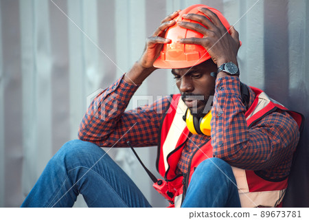 African American male technician or engineer. Sit near a container and look tired and sleepy or unemployed. Logistics industrial cargo mover concept. 89673781
