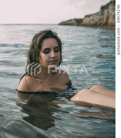 Elegant woman sit in the water. Sunset. The concept of unity with nature. Elegant woman sit in the water. Sunset. The concept of unity with nature. 89674246