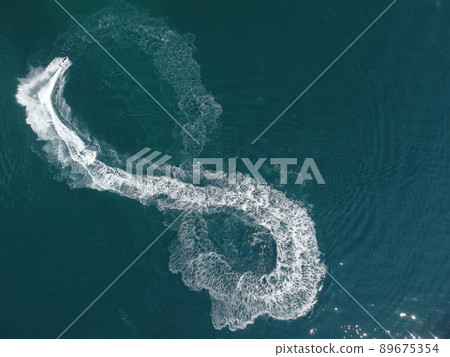 Aerial top down view of water foam trace with nice deep blue shade of ocean. Beautiful white trail on the calm sea surface behind a small powerful motorboat. Propwash. Summer vacation travel concept Aerial top down view of water foam trace with nice deep blue shade of ocean. Beautiful white trail on the calm sea surface behind a small powerful motorboat. Propwash. Summer vacation travel concept 89675354