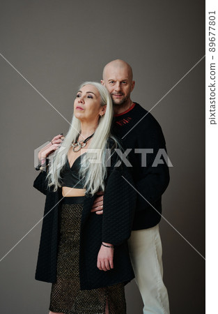 Vertical medium long studio portrait of modern mature Caucasian couple wearing stylish clothes posing on camera, gray background Vertical medium long studio portrait of modern mature Caucasian couple wearing stylish clothes posing on camera, gray background 89677801