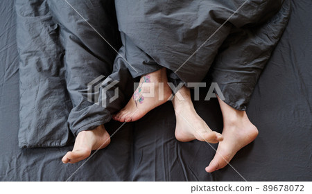 Top-down shot of modern unrecognizable romantic couple feet uncovered in bed in morning, gray bed linen Top-down shot of modern unrecognizable romantic couple feet uncovered in bed in morning, gray bed linen 89678072