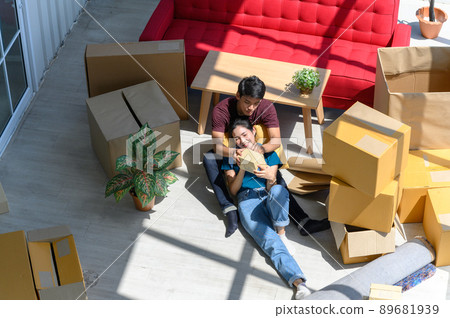 Top view of young couple smiling, relaxing and resting on the floor after unpacking cardboard boxes in new house with cardboard boxes on floor Top view of young couple smiling, relaxing and resting on the floor after unpacking cardboard boxes in new house with cardboard boxes on floor 89681939