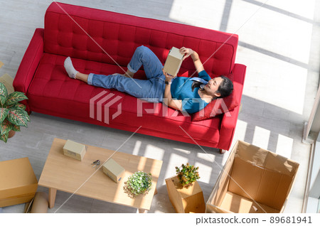 Top view of young asian women smiling, relaxing and resting on comfortable couch after unpacking cardboard boxes in new house with cardboard boxes on floor Top view of young asian women smiling, relaxing and resting on comfortable couch after unpacking cardboard boxes in new house with cardboard boxes on floor 89681941