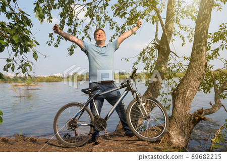 Happy adult man with bicycle near the river, active recreation concept Happy adult man with bicycle near the river, active recreation concept 89682215