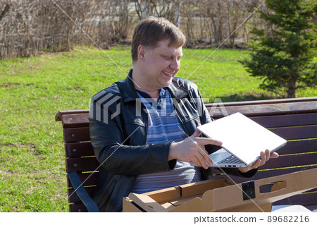 Adult blond man opens a new computer to work on the street Adult blond man opens a new computer to work on the street 89682216