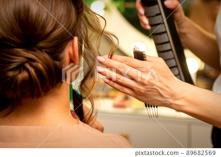 Professional hairdresser styling and fixing with hairspray long woman curly hair in a beauty salon 89682569