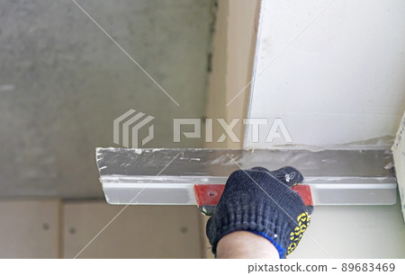 The master's hand levels the wall with a spatula, applying the plaster mixture to the wall. The master's hand levels the wall with a spatula, applying the plaster mixture to the wall. 89683469