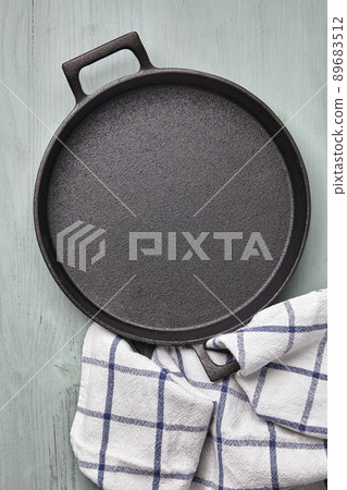 Empty round cast iron pan, tea towel on a light blue wooden table 89683512