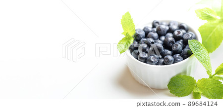 Advertising banner for natural healthy food. White bowl with forest blueberries and fresh green mint leaves on white. Blueberry - natural superfood. Close up. Copy space for text or design. 89684124