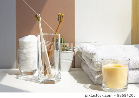 Bathroom, toothbrushes in a glass on which the sun's rays fall, white cotton towels, green cactus, personal hygiene products. Bathroom, toothbrushes in a glass on which the sun's rays fall, white cotton towels, green cactus, personal hygiene products. 89684203