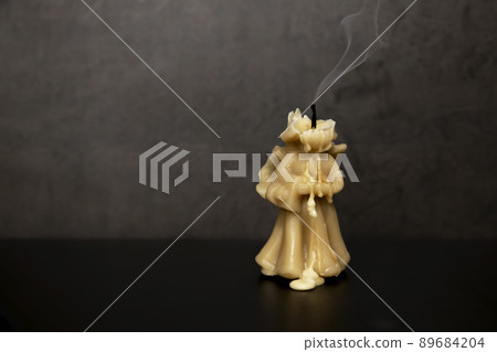 Wax candle, Yellow candle in the form of an extinguished angel extinguished, smoke from the oppression to the top. Wax candle, Yellow candle in the form of an extinguished angel extinguished, smoke from the oppression to the top. 89684204