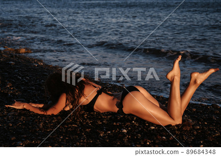 brunette girl with a sexy ass is lying sunbathing on the beach by the sea in summer 89684348