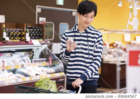 A young man shopping while looking at a smartphone at a supermarket A young man shopping while looking at a smartphone at a supermarket 89684567