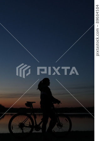 Silhouette of woman with mountain bike on colorful blue sky sunset background. Active outdoors lifestyle Silhouette of woman with mountain bike on colorful blue sky sunset background. Active outdoors lifestyle 89684584