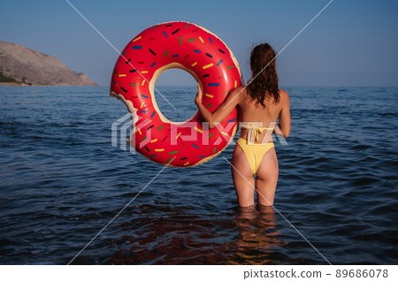 slender woman with a sexy booty in a swimsuit holds an inflatable circle in her hands on a sunny summer day 89686078