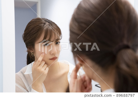 A woman checking her skin in the mirror A woman checking her skin in the mirror 89688797