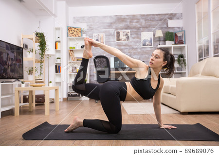 Young brunette doing exercise for balance on yoga mat in home. 89689076