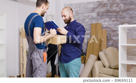 Man from delivery service arriving with boxes and documents to be signed. Beautiful young couple moving in. Man from delivery service arriving with boxes and documents to be signed. Beautiful young couple moving in. 89689111