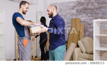 Man from delivery service arriving with boxes and documents to be signed. Beautiful young couple moving in. 89689113