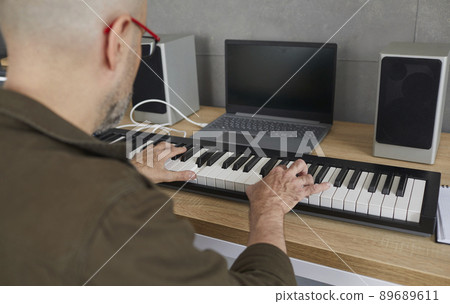 Man is rehearsing while playing on compact modern synthesizer in his home music studio. Man is rehearsing while playing on compact modern synthesizer in his home music studio. 89689611