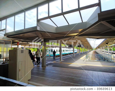 A blue character train that stops at the left end of a platform with many children. The sky can be seen from the overhead glass window. A blue character train that stops at the left end of a platform with many children. The sky can be seen from the overhead glass window. 89689613