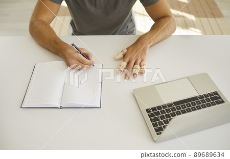 Man wearing braces on his broken fingers sitting at desk and writing in notebook 89689634