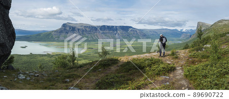 Panoramic scenic view of glacial Rapadalen river delta valley with lonely hiker figure, Skierffe rock summit at Sarek national park, meanders, lakes, blue mountains, forest. Summer landscape Sweden Panoramic scenic view of glacial Rapadalen river delta valley with lonely hiker figure, Skierffe rock summit at Sarek national park, meanders, lakes, blue mountains, forest. Summer landscape Sweden 89690722