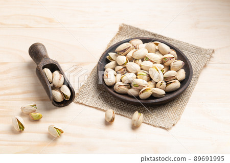 Pistachios on wooden spoon and dish on light wooden base. 89691995