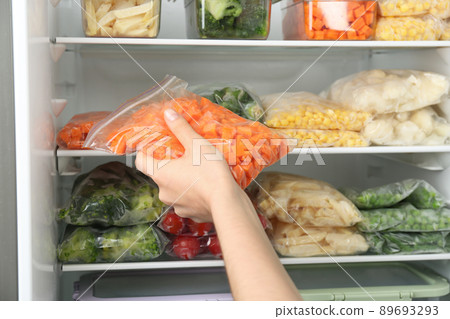 Woman putting plastic bag with carrot in refrigerator with frozen vegetables, closeup Woman putting plastic bag with carrot in refrigerator with frozen vegetables, closeup 89693293