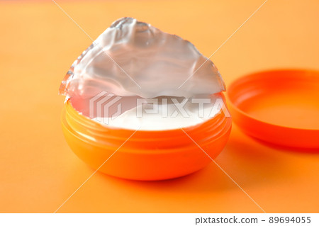 cream in a orange color container on orange background  89694055