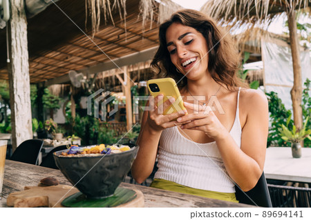 Joyful woman browsing smartphone in tropical cafe Joyful woman browsing smartphone in tropical cafe 89694141