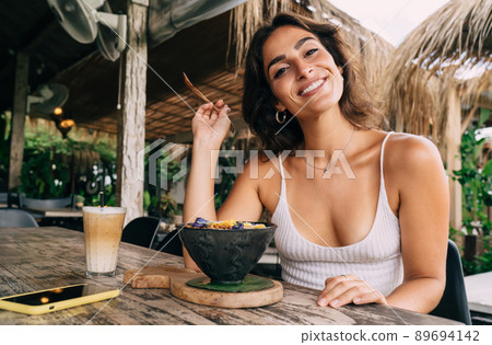 Ethnic woman with toothy smile eating in tropical resort Ethnic woman with toothy smile eating in tropical resort 89694142