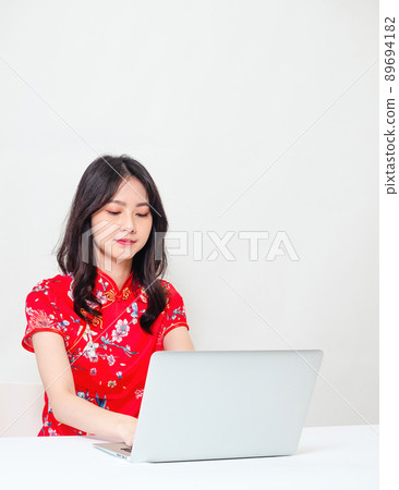 Portrait of a young asian woman in traditional cheongsam qipao dress using laptop on white background. Portrait of a young asian woman in traditional cheongsam qipao dress using laptop on white background. 89694182